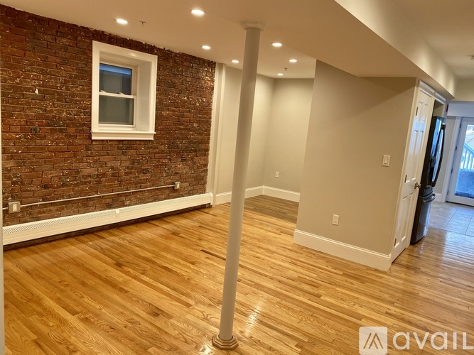A room with wooden floors and a brick wall with a window.