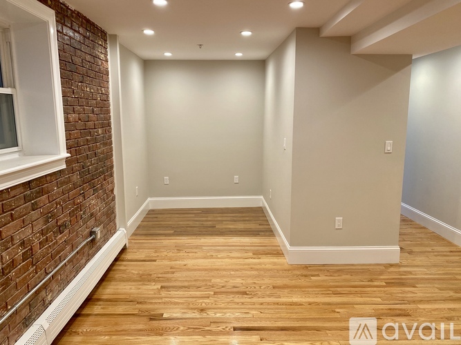 A room with wooden flooring and a brick wall on the left side.