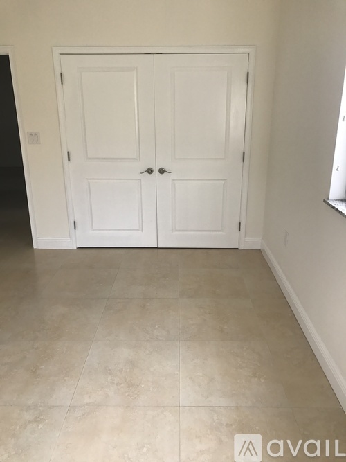 A white double door with a black handle is in a room with a tiled floor.