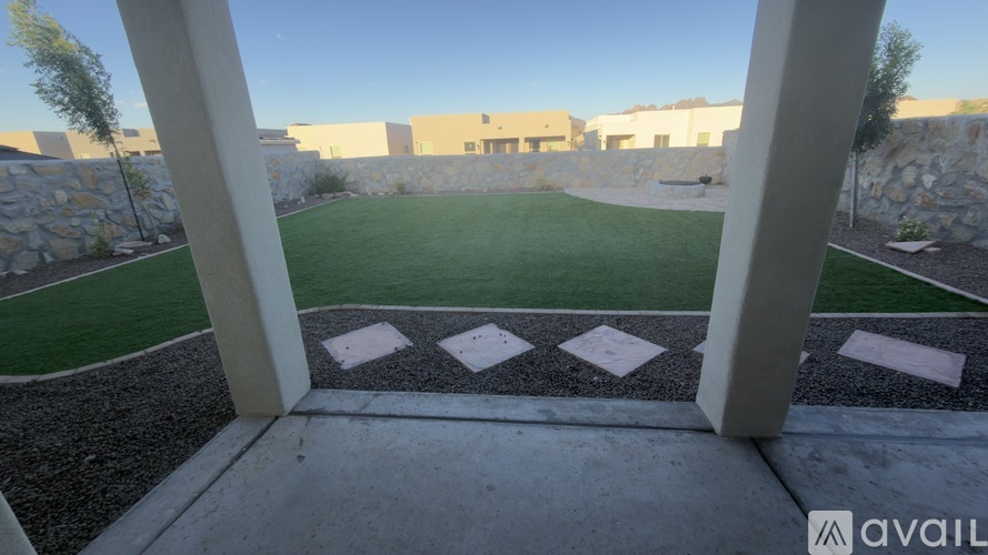 A view of a green lawn through a window with a stone wall and buildings in the background.