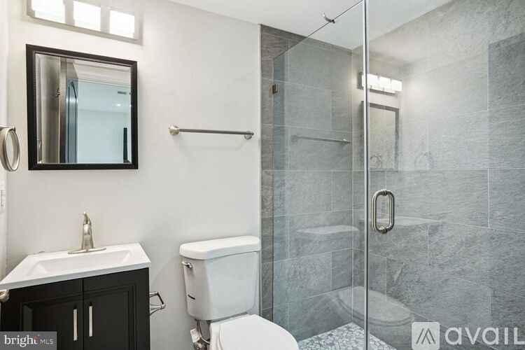 A bathroom with a toilet, sink, mirror, and shower.