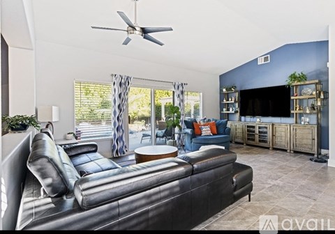A living room with a black leather sofa and a ceiling fan.