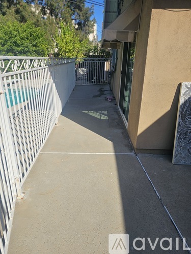 A narrow sidewalk runs between a white fence and a tan building.