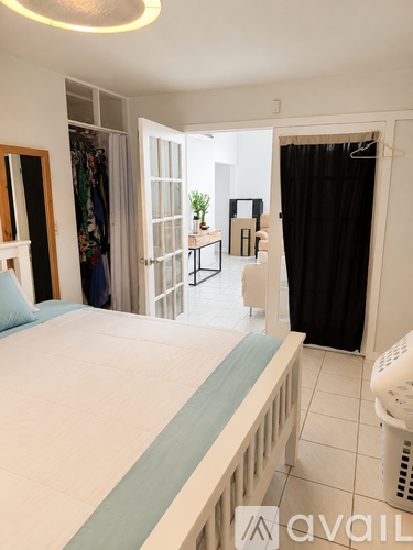A bedroom with a large bed and a wardrobe with clothes hanging in it.