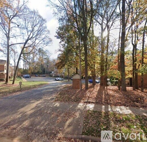 A tree-lined street with a sidewalk and cars parked on the side.