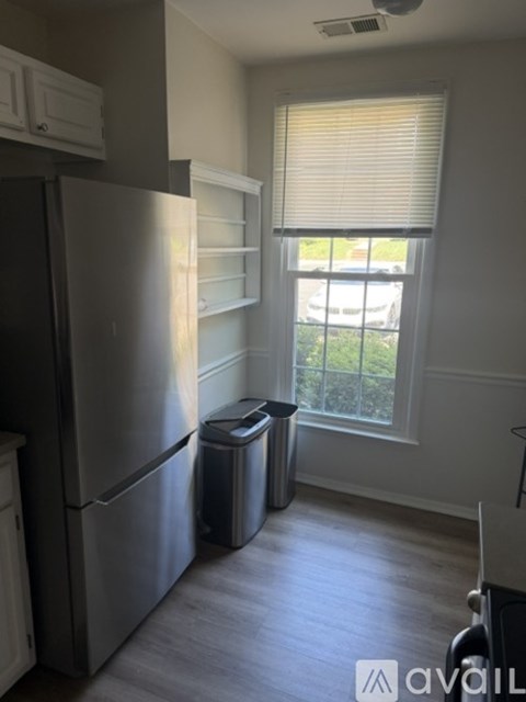 A kitchen with a stainless steel refrigerator and a window with blinds.
