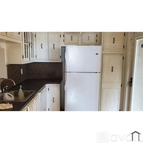A white refrigerator stands in a kitchen with white cabinets and a dark countertop.