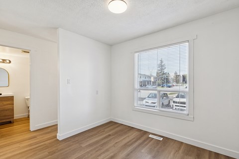 A room with a window showing a view of a parking lot and trees.