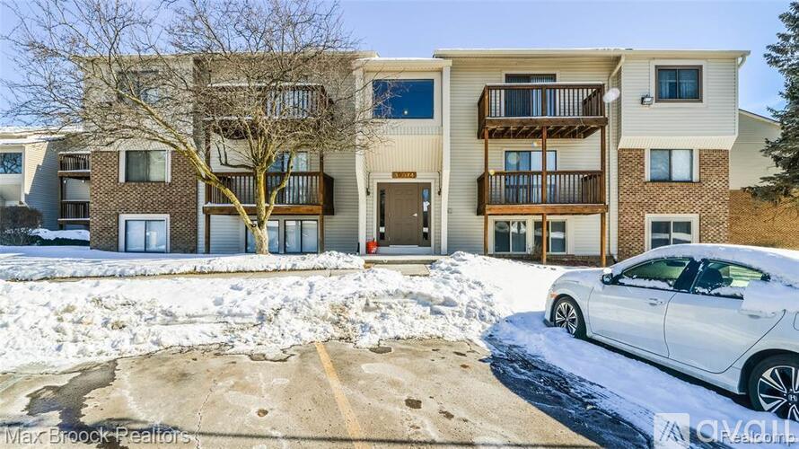 A white car is parked in front of a building with a snowy ground.
