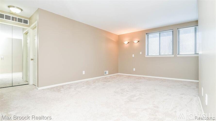 A spacious room with a carpeted floor, a window with blinds, and a door leading to another room.