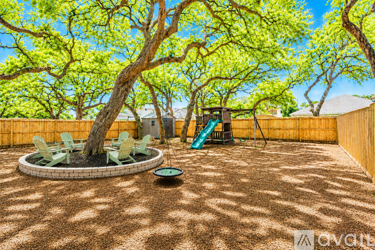 A backyard with a fire pit, chairs, and trees.
