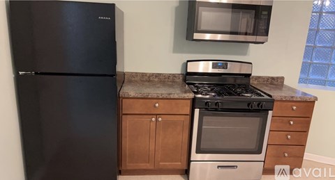 A black fridge and stove in a kitchen with a microwave and wooden cabinets.
