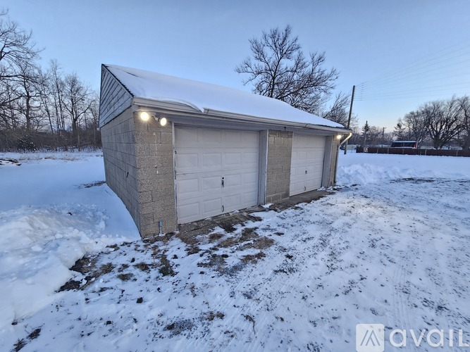 A small building with a garage door is covered in snow.