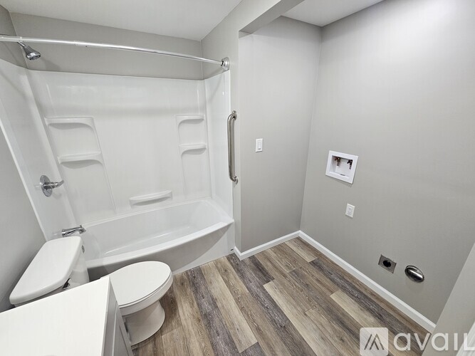 A bathroom with a white toilet and a white bathtub with a wooden floor.