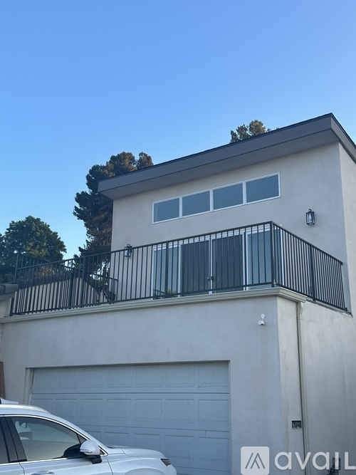 A white car is parked in front of a house with a balcony.