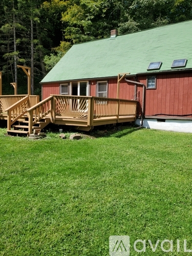 A wooden deck is in front of a red house with a green roof.