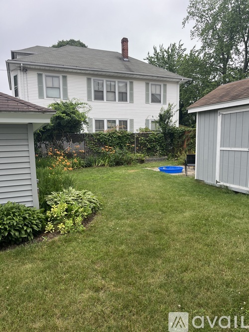 A backyard with a white house, a small pool, and a shed.