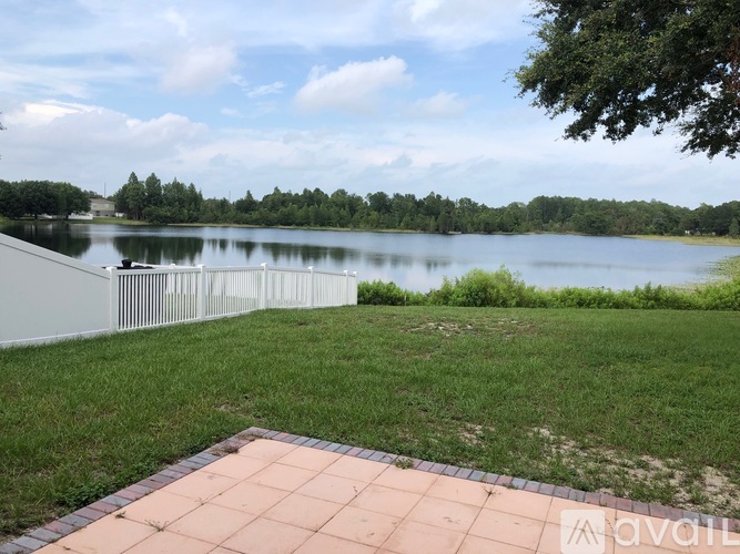 A serene lakeside scene with a clear blue sky and a white fence in the foreground.