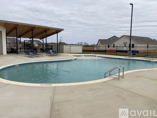 A pool with a pavement around it and a building in the background.
