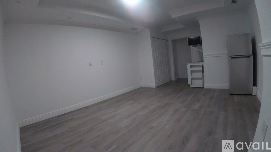 A spacious room with wooden flooring and a kitchenette in the background.