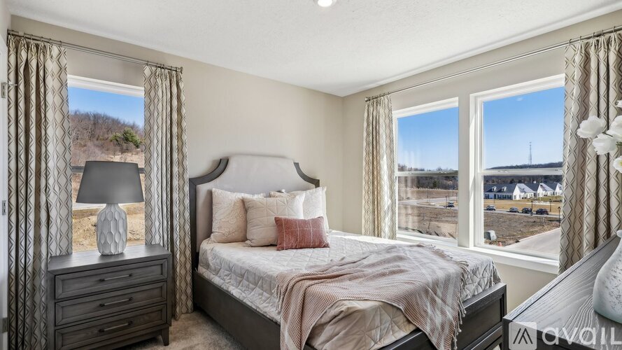 A bedroom with a large bed, a nightstand with a lamp, and a window with a view of the outside.