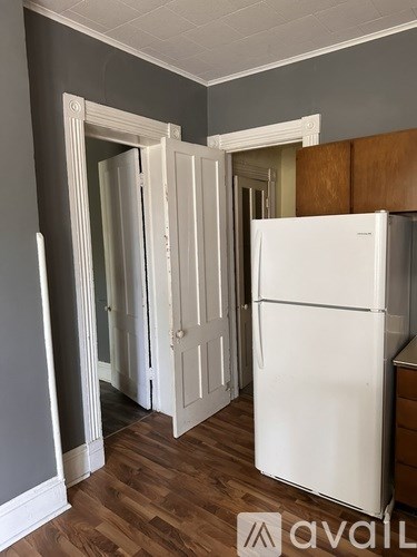 A white refrigerator in a kitchen with wooden floors and grey walls.