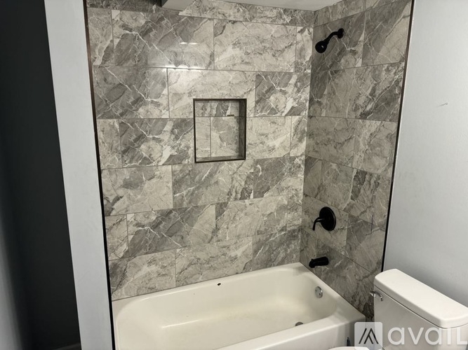 A bathroom with a marble tile wall and a white bathtub.