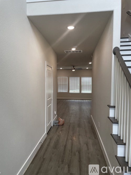 A hallway with a staircase on the right and a window with blinds on the left.