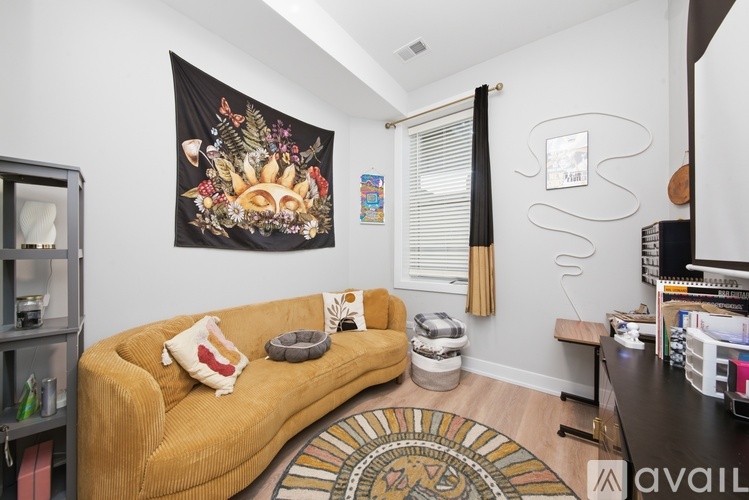 A living room with a mustard colored couch and a tapestry hanging on the wall.
