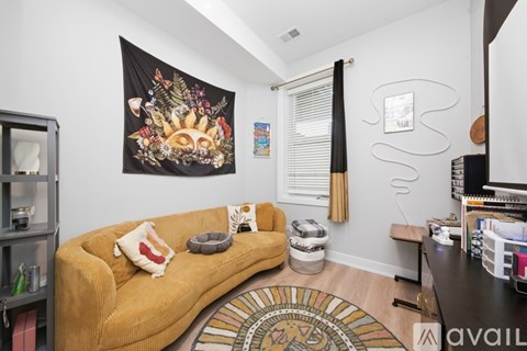 A living room with a mustard colored couch and a tapestry hanging on the wall.