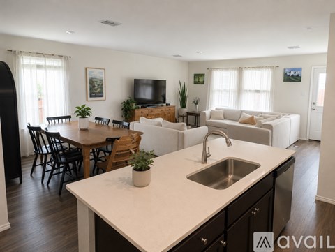 A kitchen with a sink, a dining table and chairs, and a living room with a couch and a television.