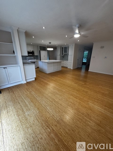 A spacious kitchen with wooden flooring and white cabinetry.