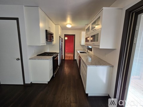 A kitchen with white cabinets and a red door.