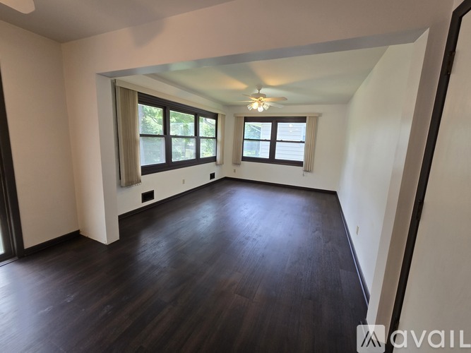 A spacious room with dark wood flooring and white walls.