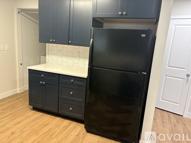 A black refrigerator is in a kitchen with wooden floors and white cabinets.