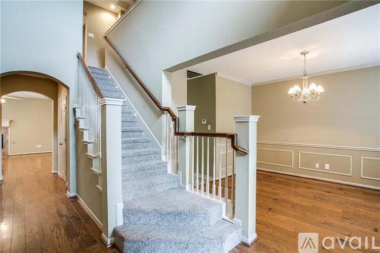A staircase with a wooden banister and a grey carpeted runner leads up to a landing with a chandelier.