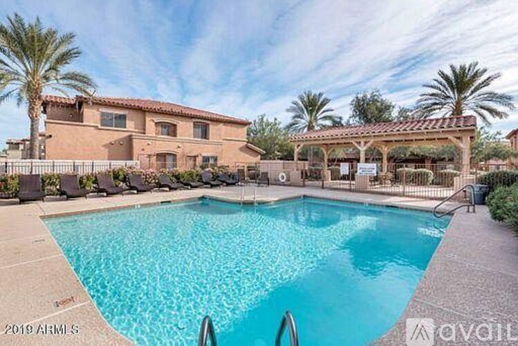 A large swimming pool in front of a house with a patio and palm trees.