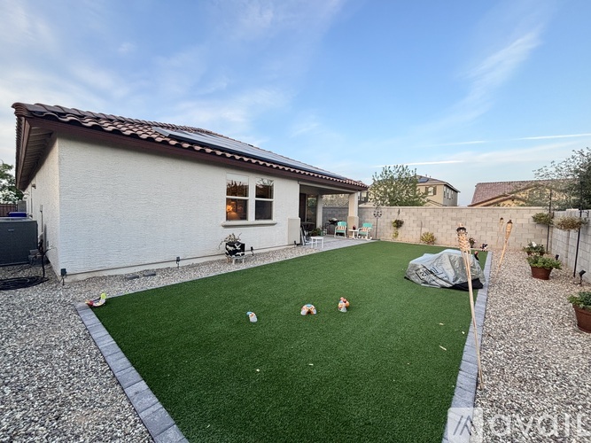 A house with a white exterior and a brown roof has a small garden with artificial grass and a few toys scattered around.