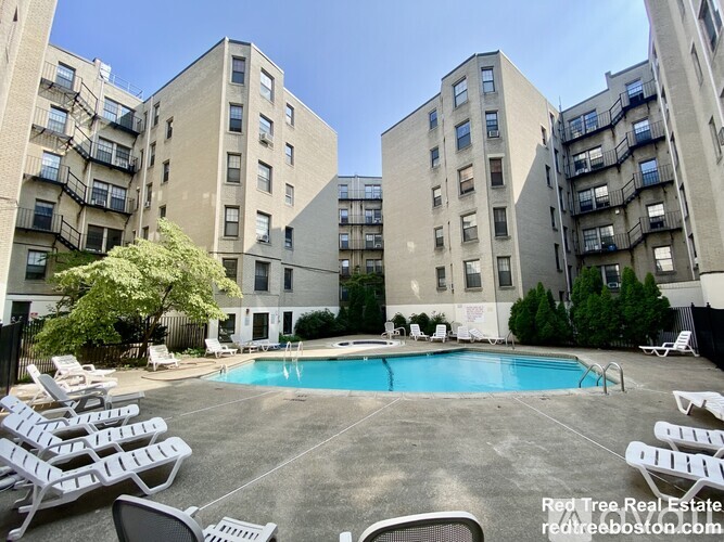 A swimming pool surrounded by lounge chairs in a courtyard of apartment buildings.