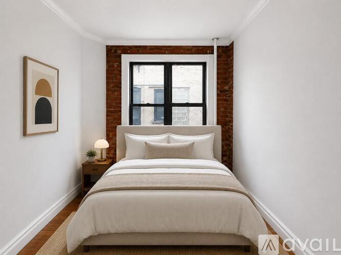 A bedroom with a bed, nightstand, and a window with a brick wall.