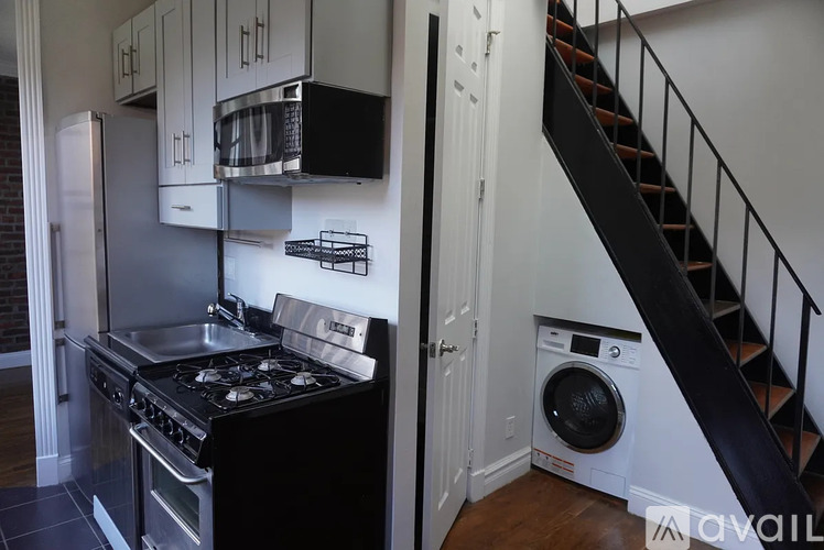 A kitchen with a stove top oven and a washing machine under a staircase.