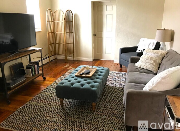 A living room with a television, a chair, a sofa, and a footstool.