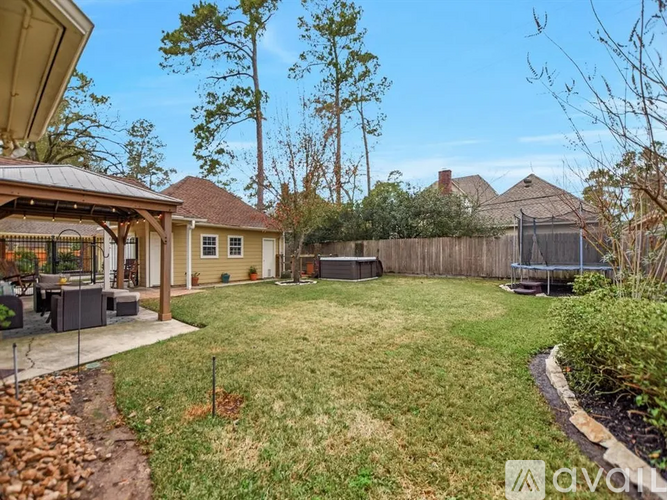 A backyard with a fence, a trampoline, and a gazebo.