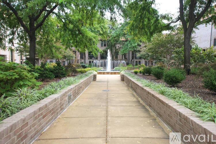 A walkway with a brick wall on either side leads to a fountain.