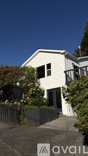 A house with a white exterior and a grey roof is surrounded by greenery.