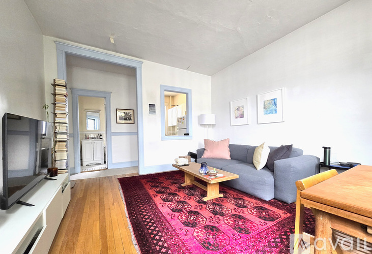 A living room with a grey couch, a red rug, and a wooden coffee table.