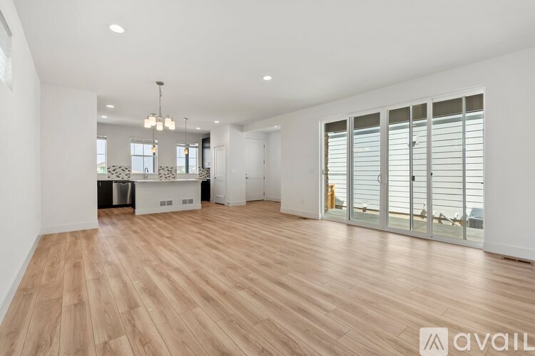 A spacious room with wooden flooring and a large window with blinds.