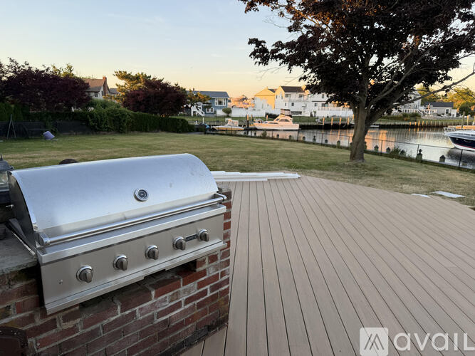 A silver grill is on a wooden deck by a tree.