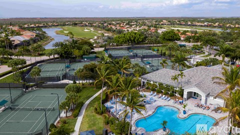 A view of a resort with a tennis court, swimming pool, and palm trees.