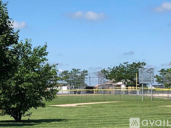 A baseball field with a fence and trees in the background.